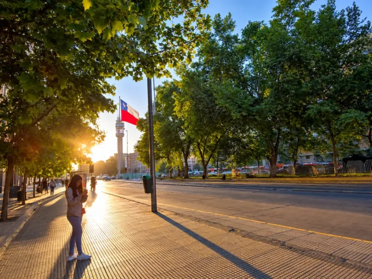 Mujer utilizando un teléfono móvil en una avenida de Santiago de Chile, con la bandera chilena al fondo, para ilustrar los resultados de América Móvil en Cono Sur.