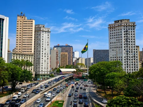 Vista urbana de São Paulo, Brasil, con edificios, avenidas transitadas y una bandera brasileña ondeando sobre el centro de la ciudad.