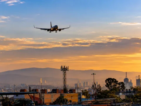 Avión en aproximación sobre una zona urbana con torres de telecomunicaciones, imagen ilustrativa de las concesiones de espectro de 800 MHz otorgadas al AICM y la Marina.